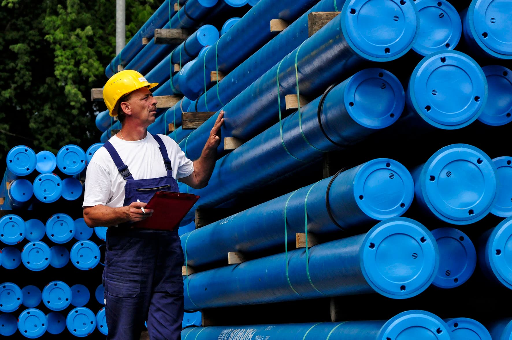Mann mit Bauhelm begutachtet Wasserrohrleitungen in einem Rohrlager.