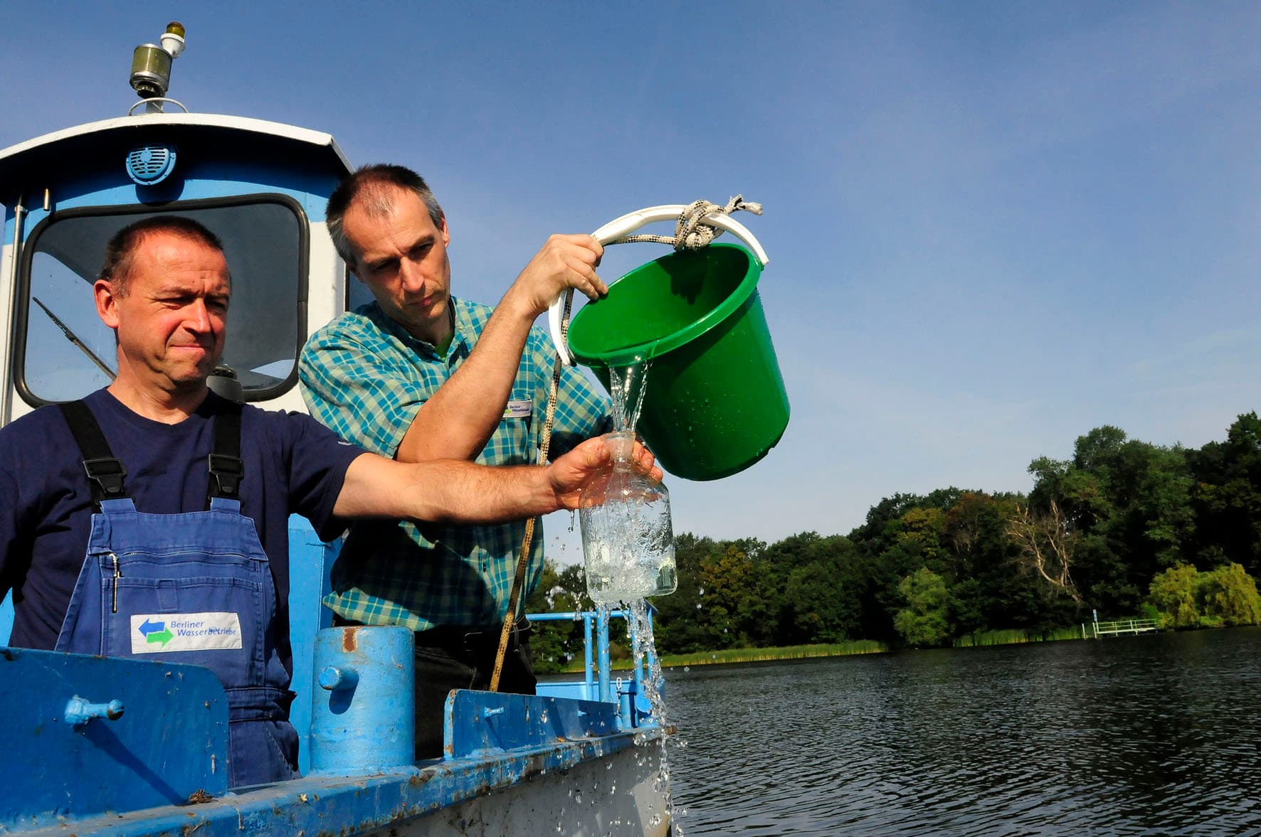 Zwei Männer nehmen Wasserproben aus einem Oberflächengewässer.