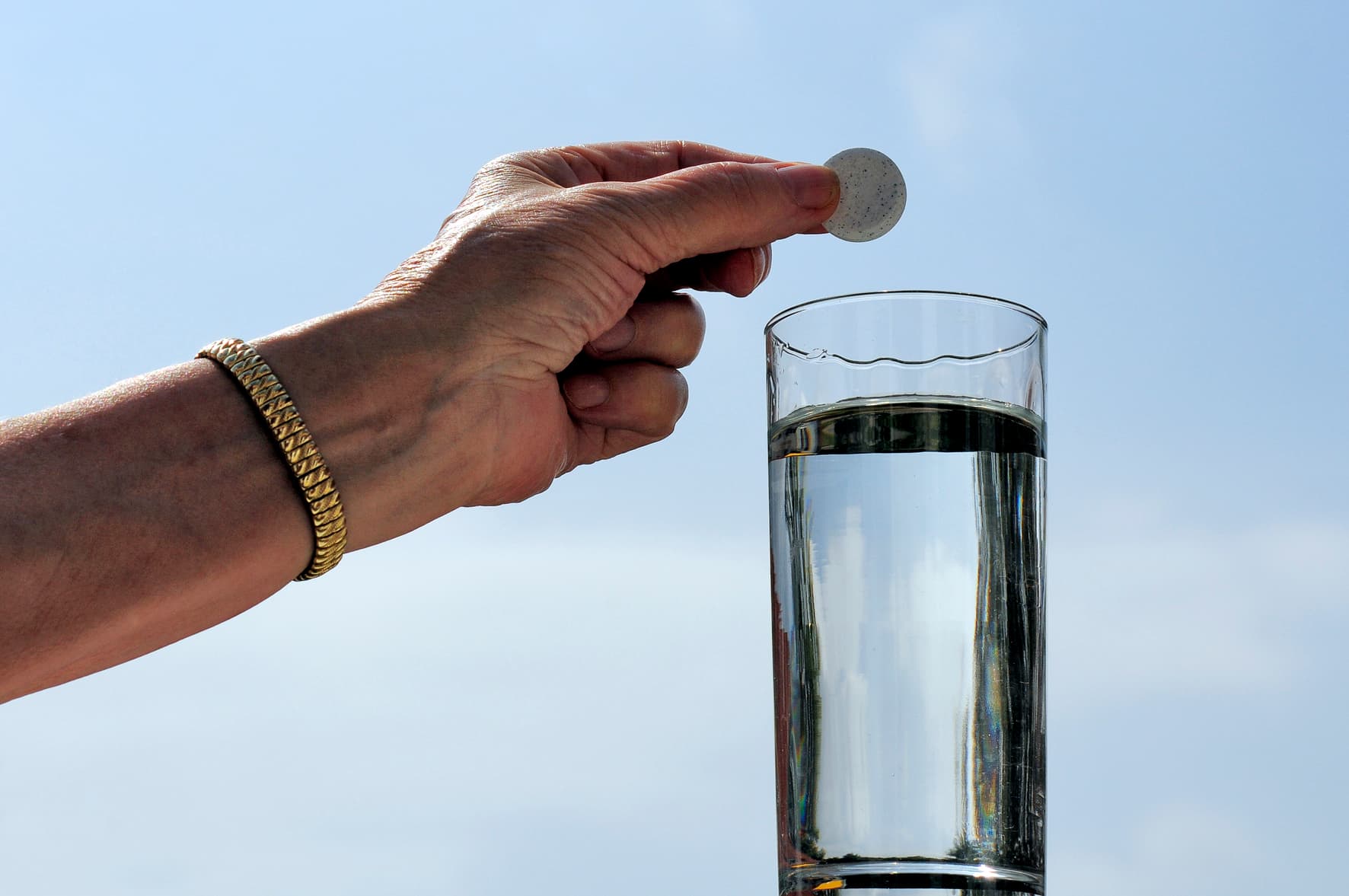 Hand gibt eine Aspirin-Tablette in ein Wasserglas.