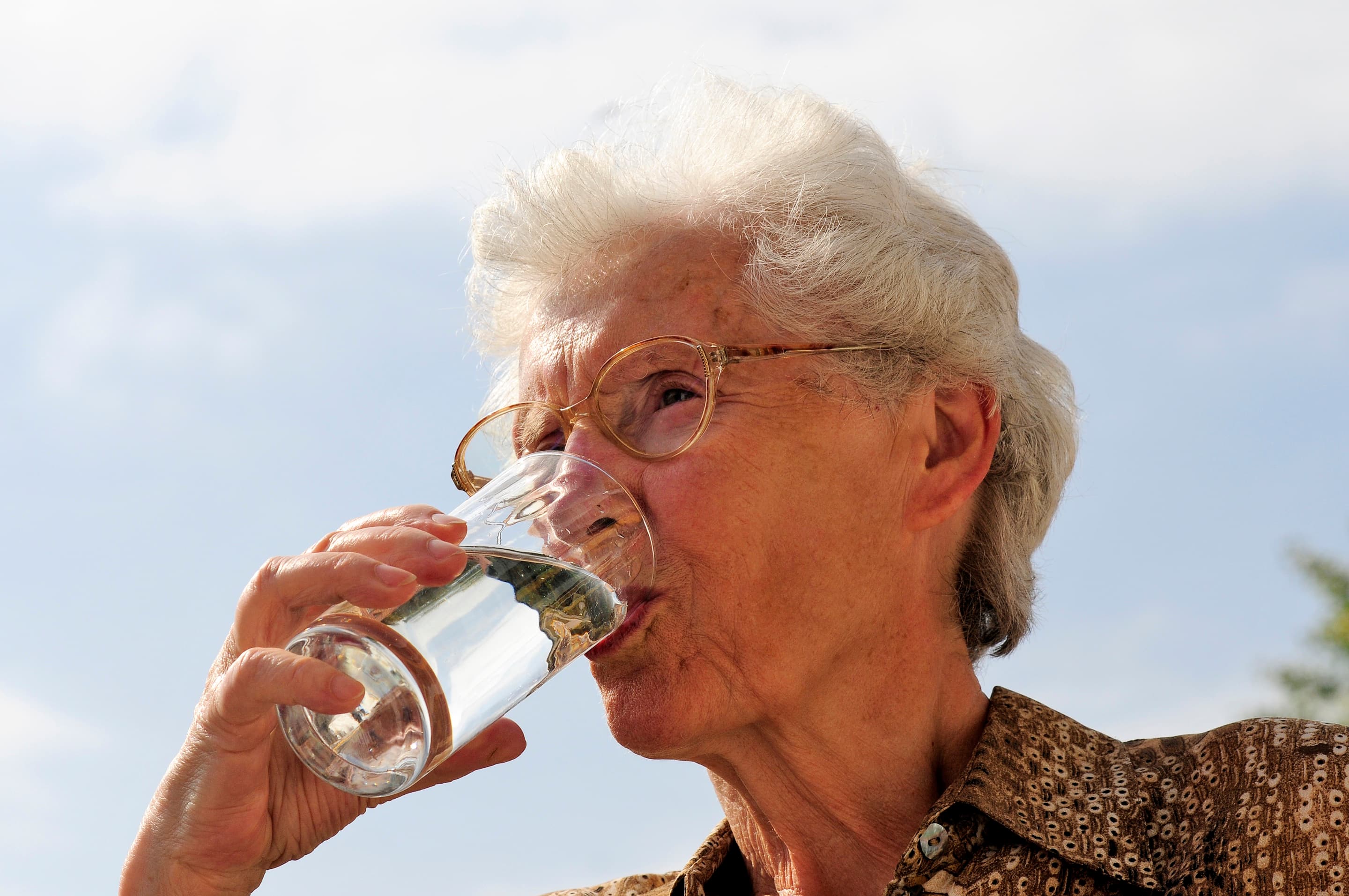 Alte Frau trinkt aus einem Wasserglas.