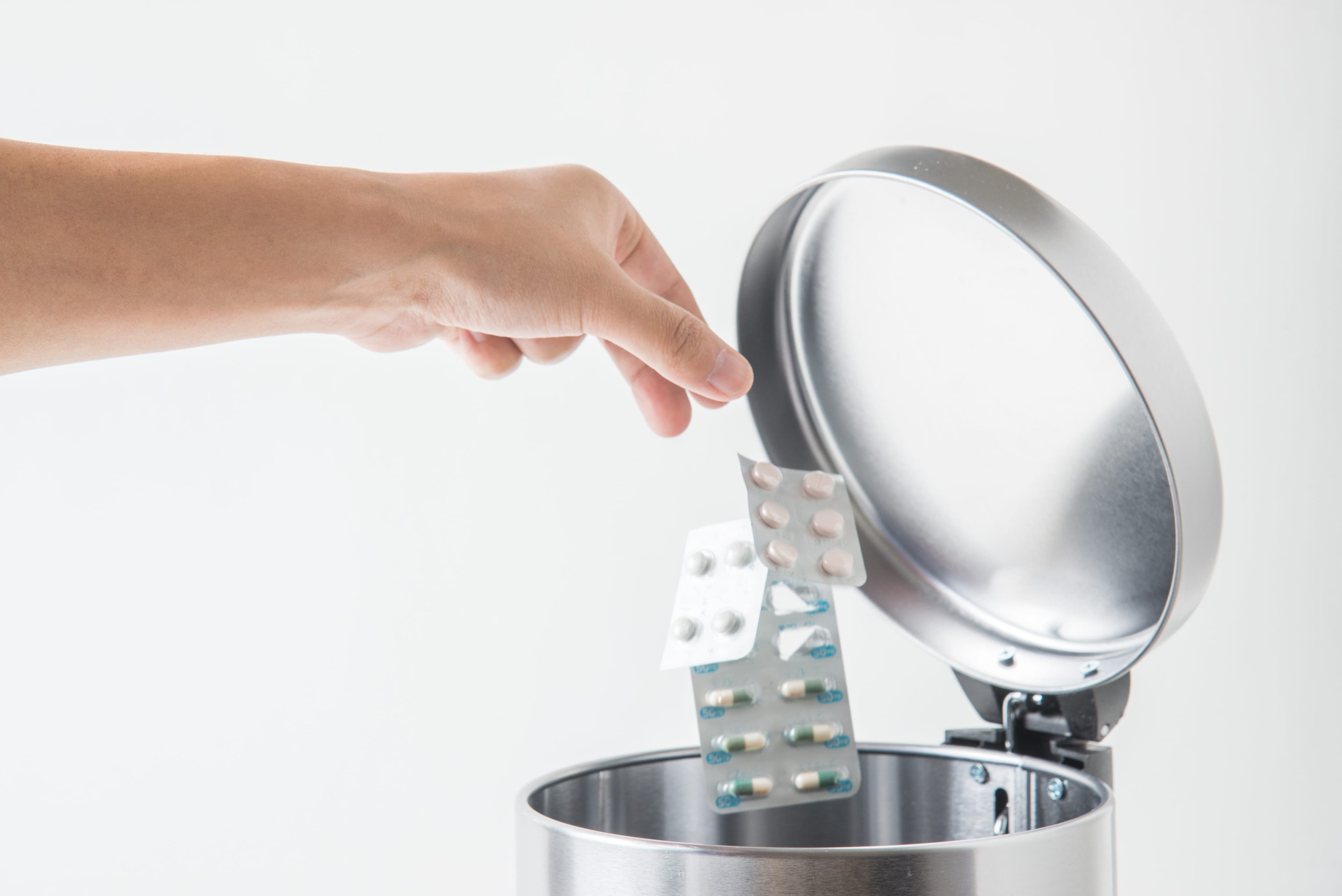 Eine Hand wirf Tablettenblister in eine Hausmülltonne.